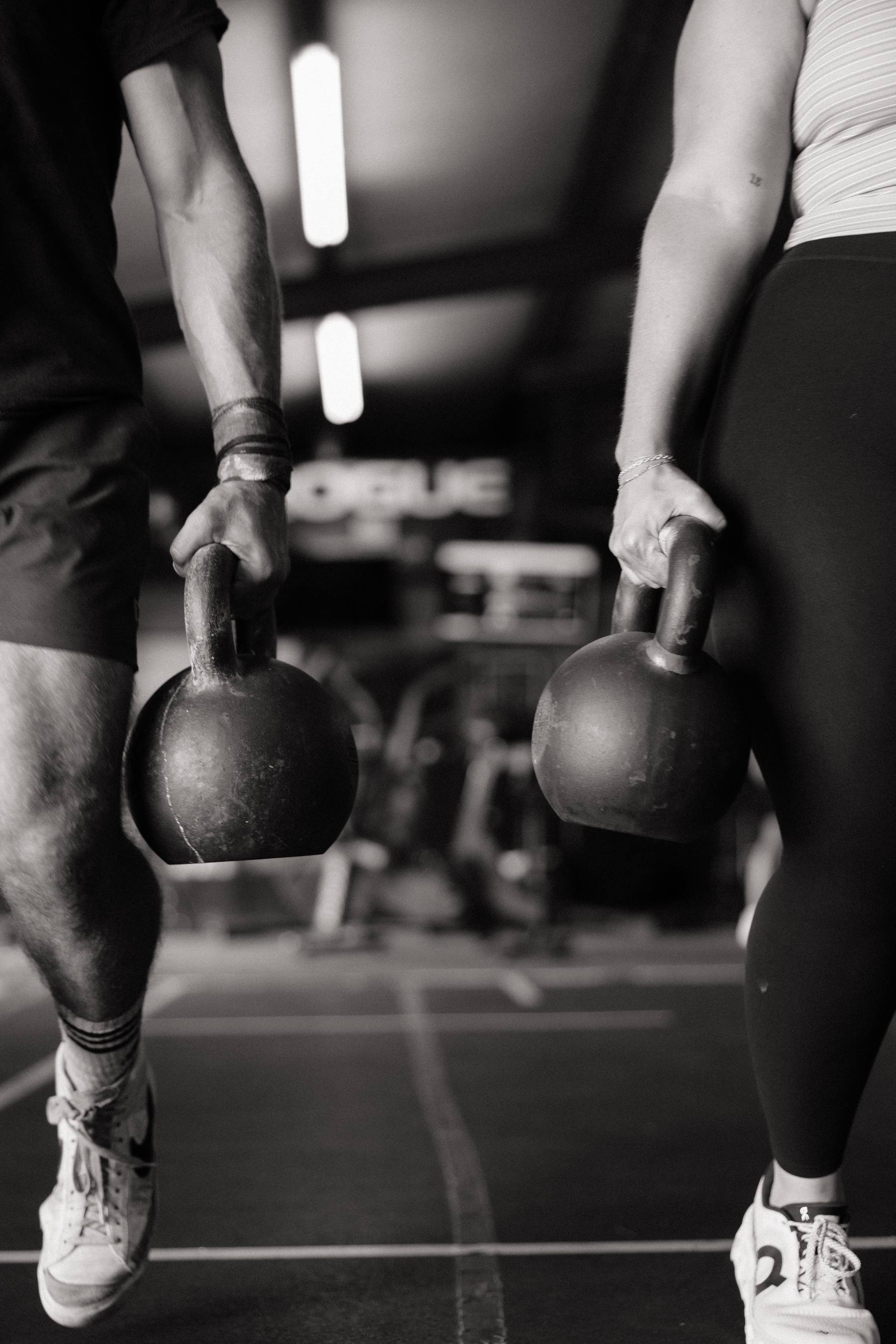 Two athletes carrying kettlebells across the floor
